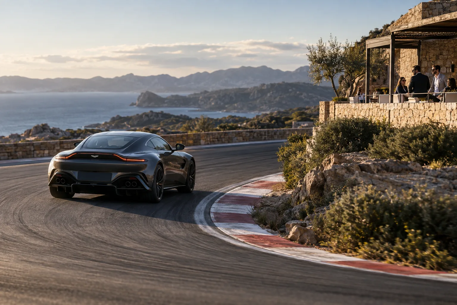 A graphite Aston Martin Vantage from a rear three-quarter angle entering a Mediterranean circuit bend