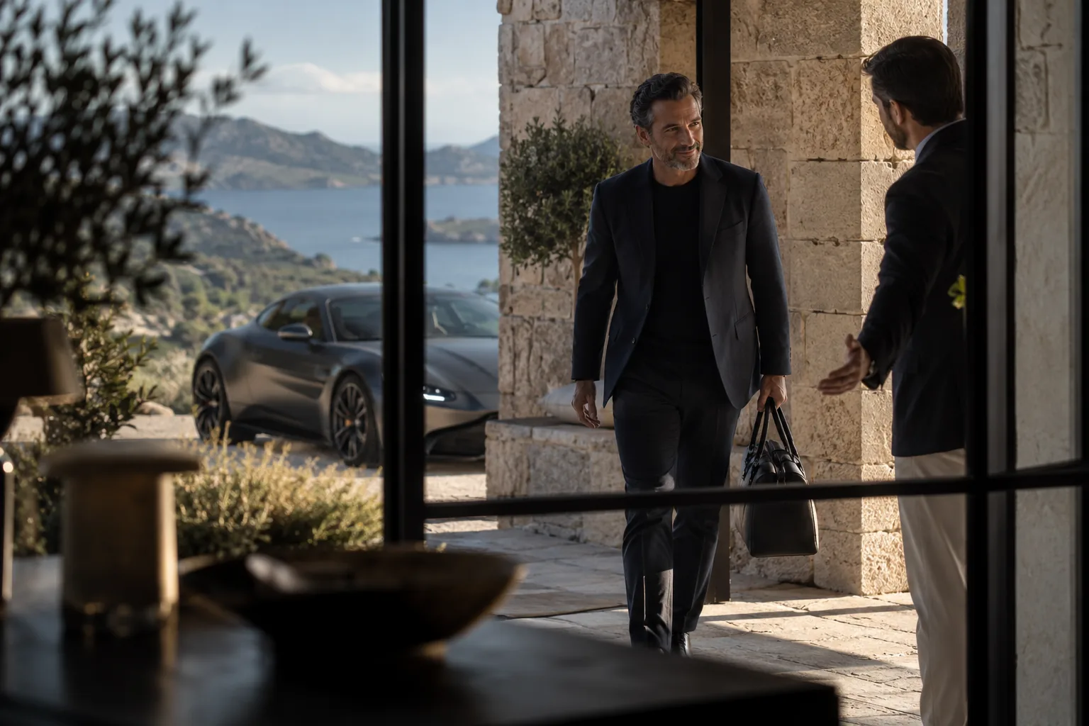 A male CEO aged 44 stepping through a shaded stone entrance with a host welcoming him